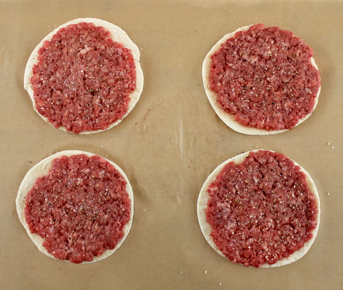 4 tortillas with ground beef smashed on top 