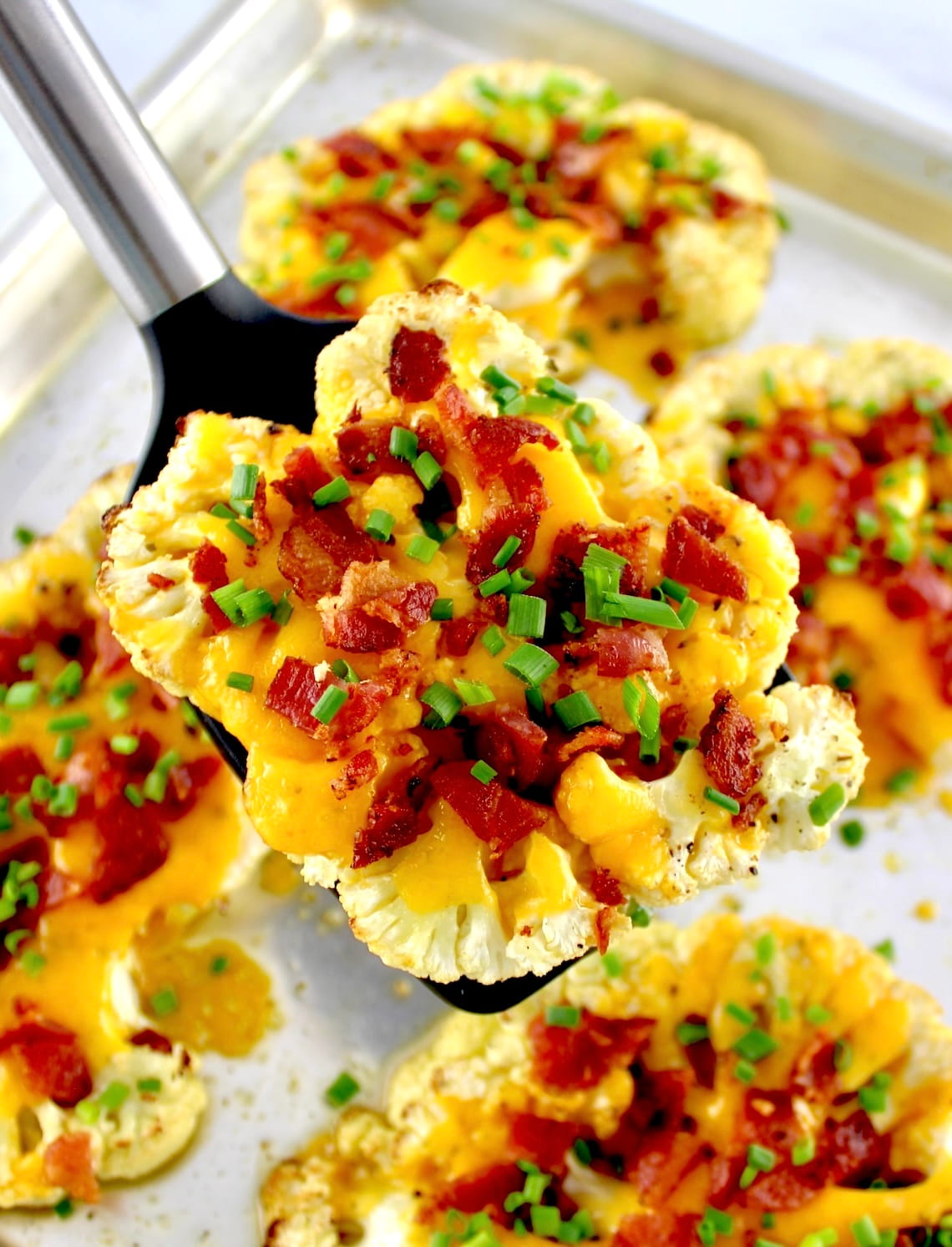spatula holding up Loaded Cauliflower Steak over baking sheet