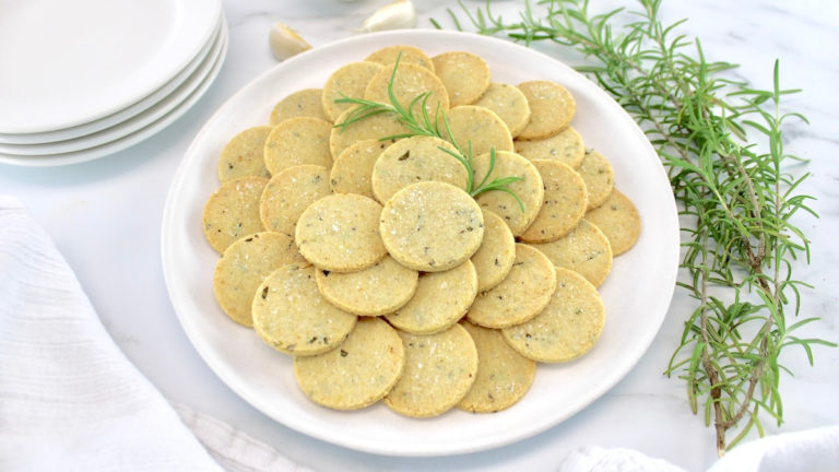 Rosemary Garlic Crackers in white bowl with rosemary and garlic in back