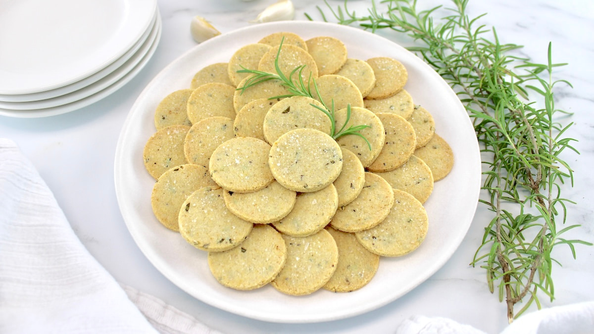 Rosemary Garlic Crackers in white bowl with rosemary and garlic in back