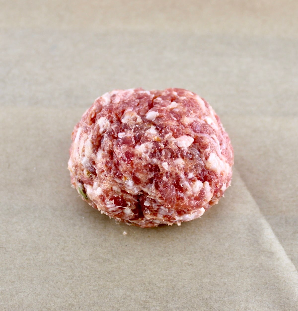 ground Italian sausage in ball on parchment paper