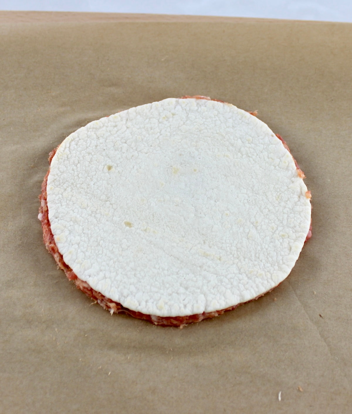 tortilla over ground Italian sausage on parchment paper
