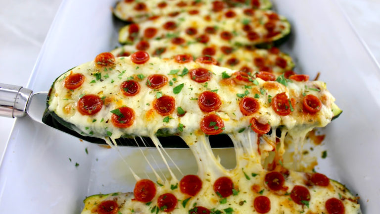 Zucchini Pizza Boat in white casserole being lifted out with spatula