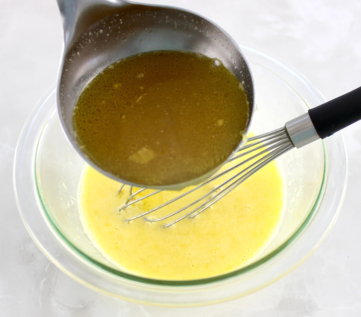 chicken broth being whisked into glass bowl with eggs and lemon