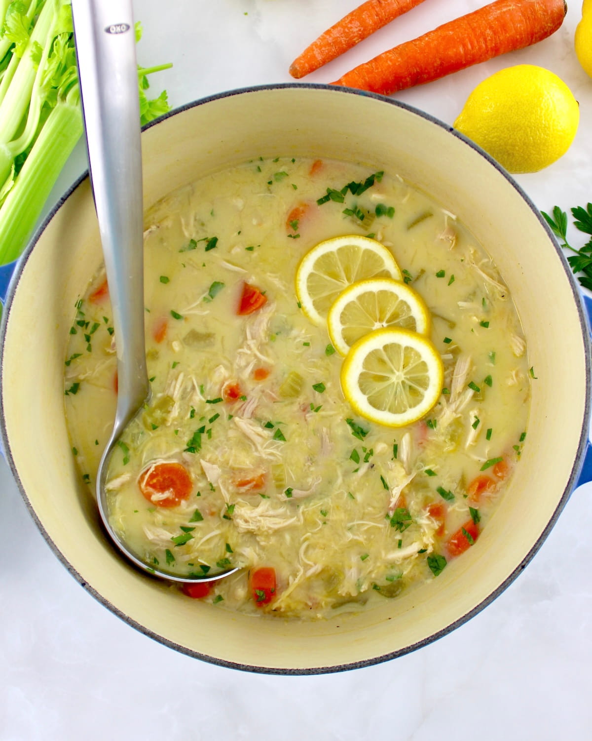overhead view of Avgolemono Soup in pot with silver ladle and 3 lemon slices