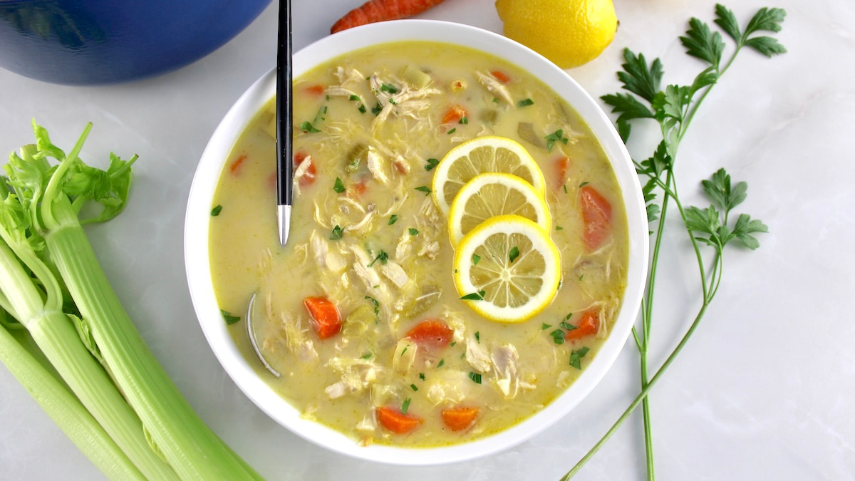 Avgolemono Soup in white bowl with spoon and 3 lemon slices on top
