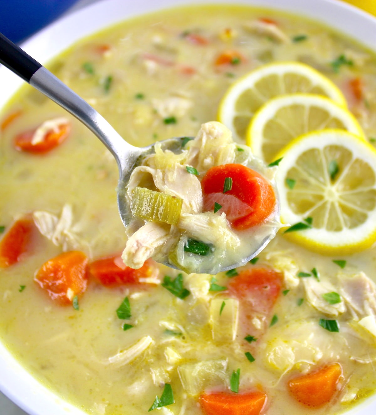 closeup of Avgolemono Soup in spoon held up over white bowl