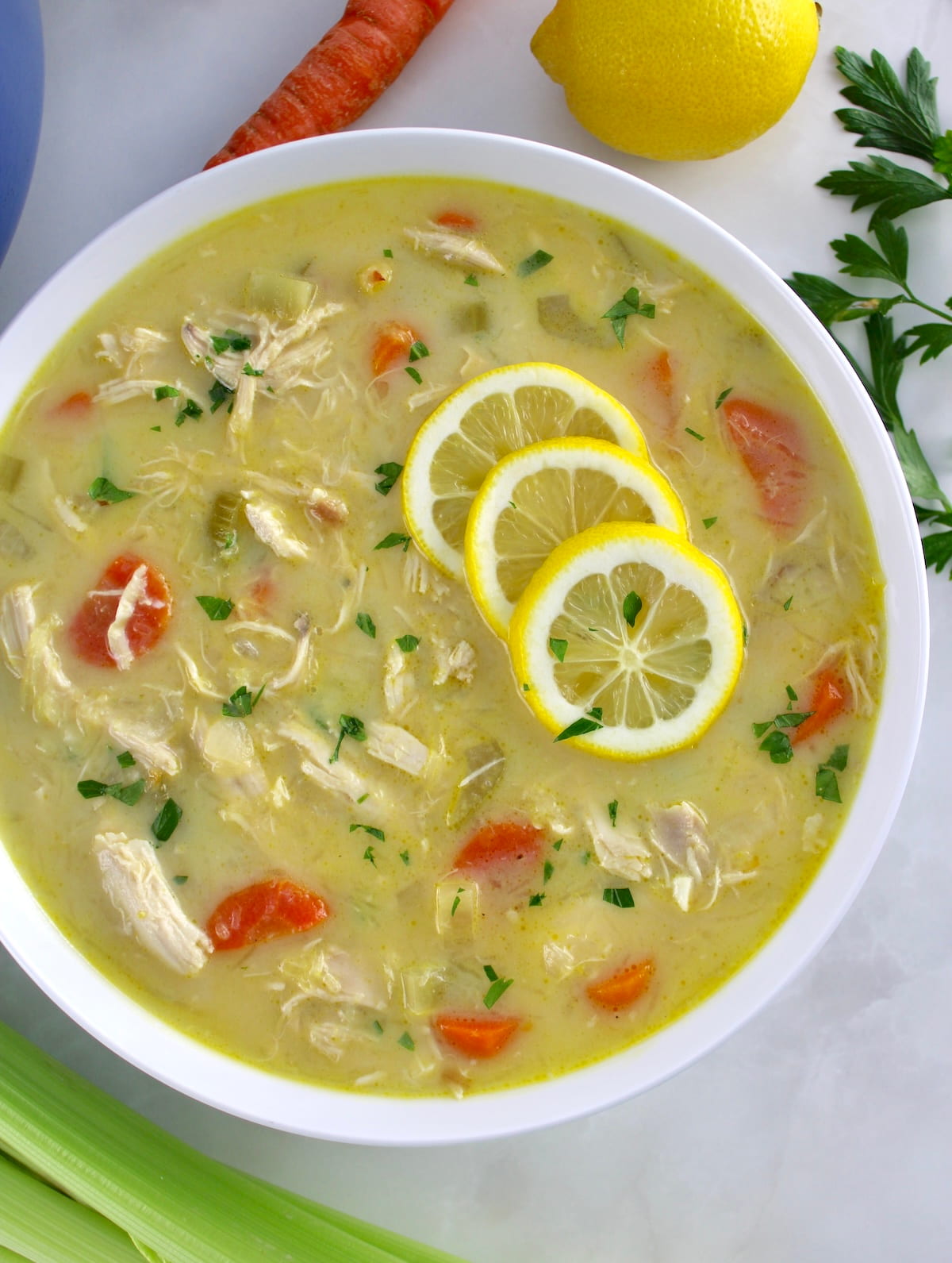 overhead view of Avgolemono Soup in white bowl with 3 lemon slices on top