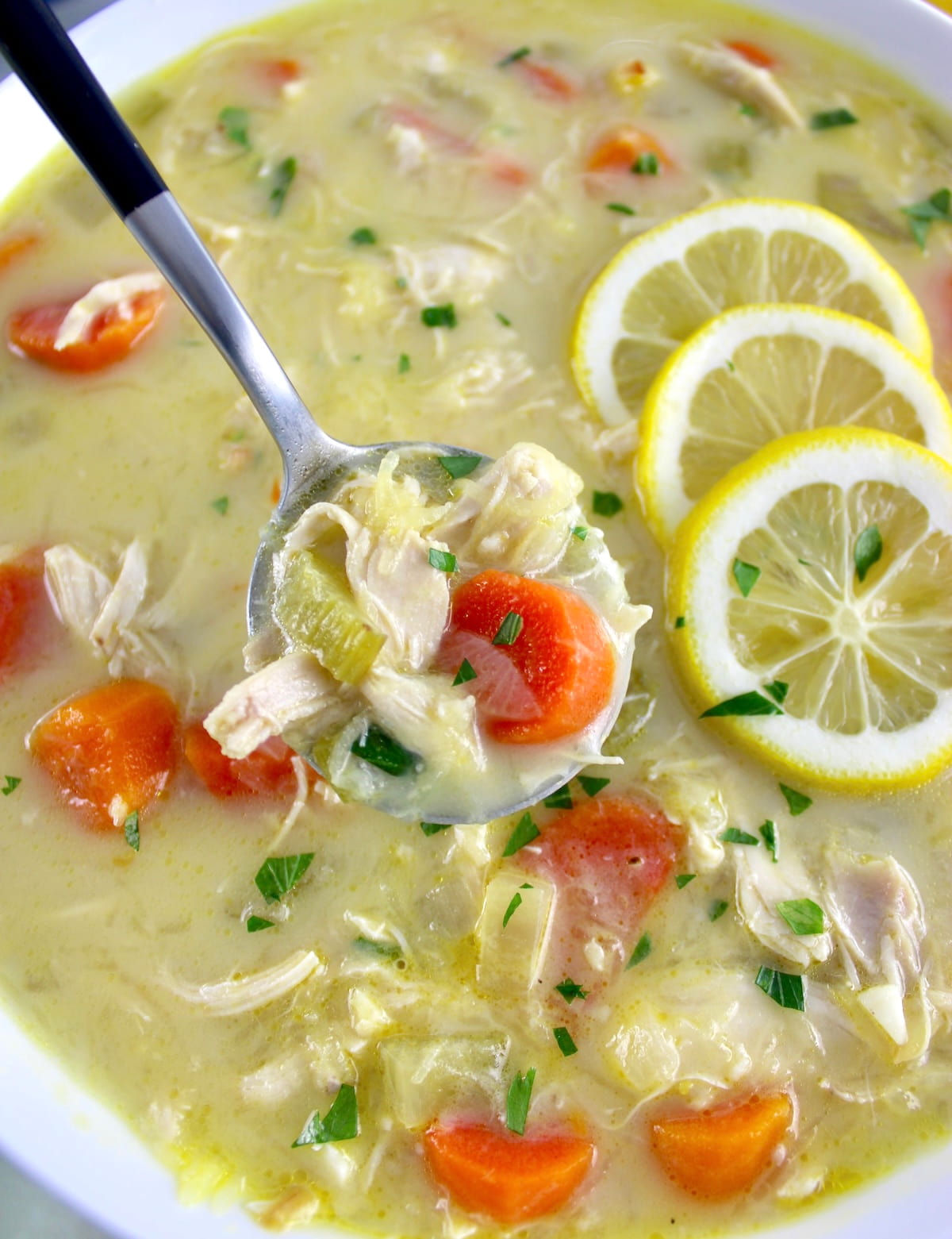 closeup of Avgolemono Soup in spoon held up over white bowl