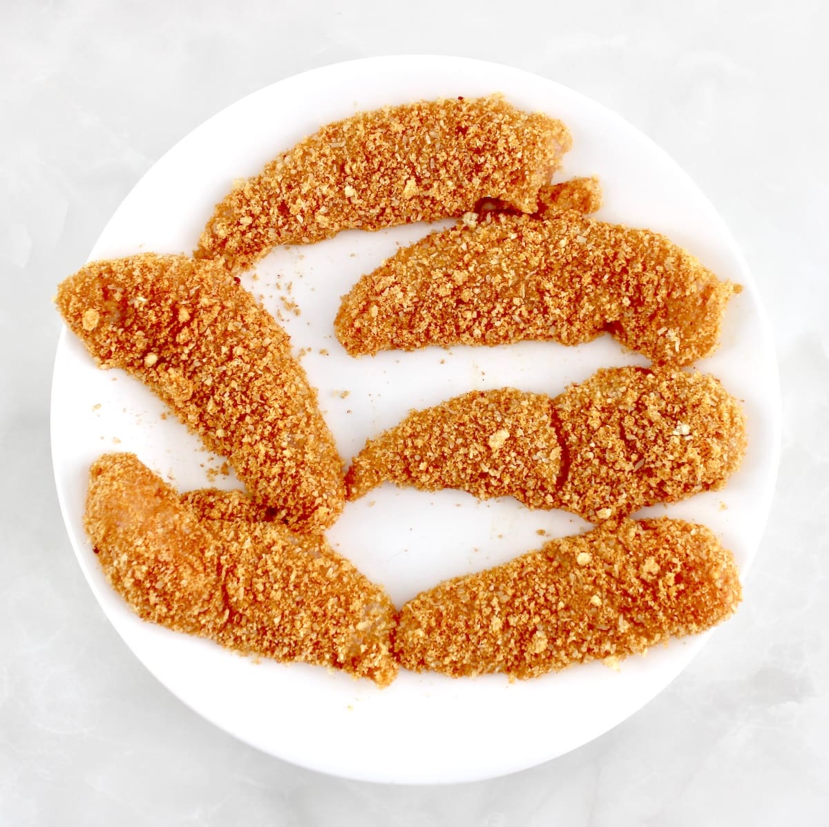 raw breaded Chicken Tenders on white plate
