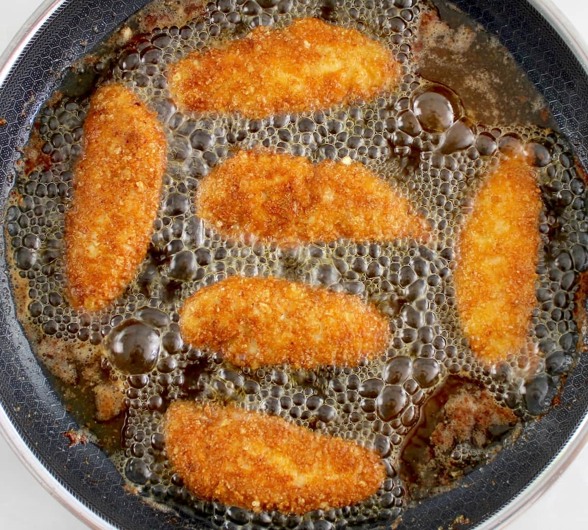 breaded chicken tenders frying in skillet