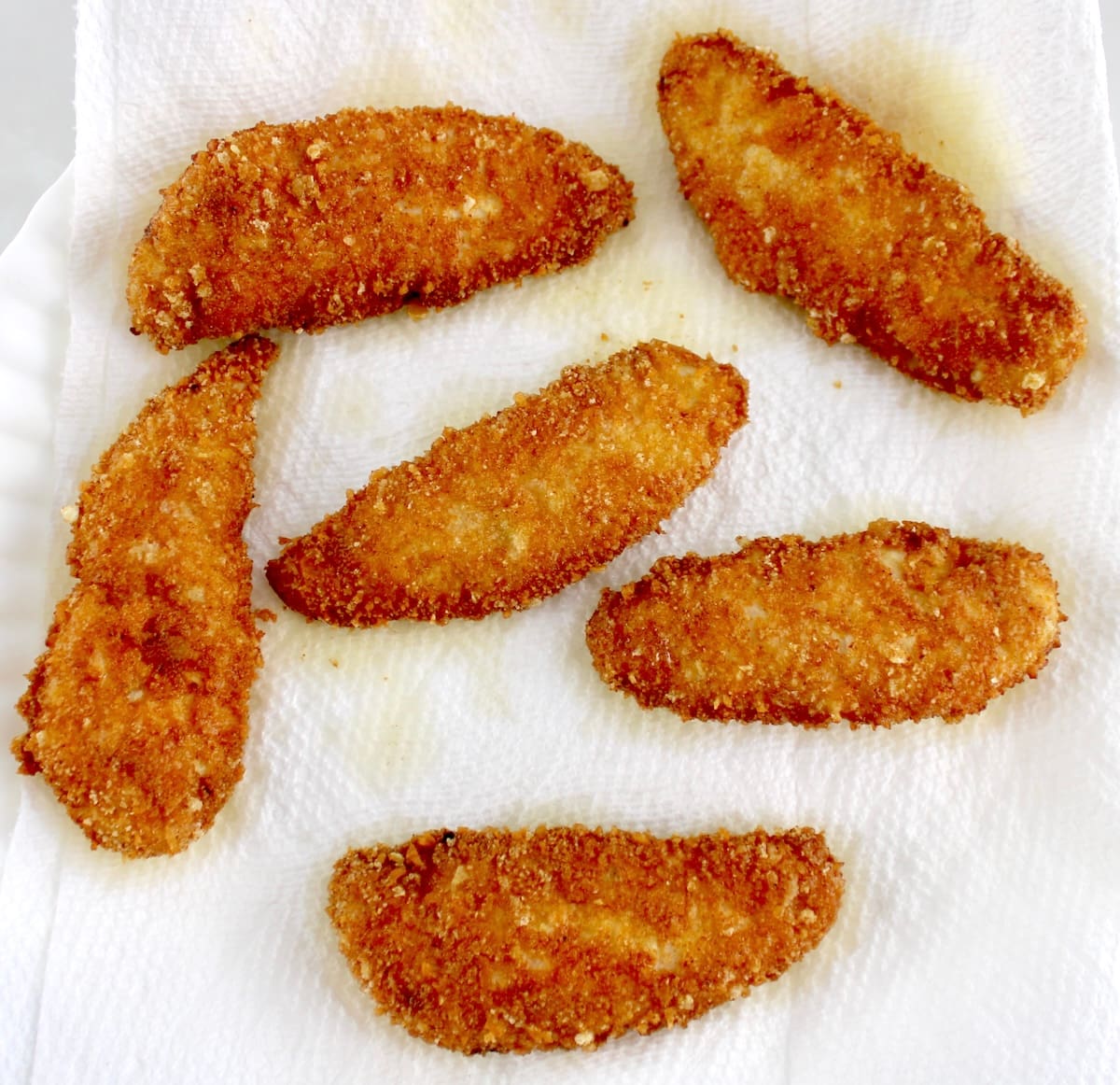 5 breaded and fried chicken tenders on paper towel lined plate