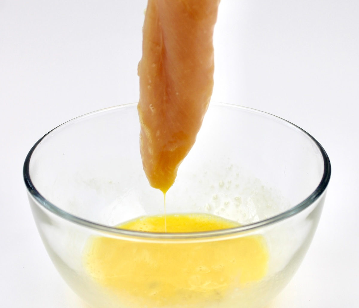 dipping chicken tender into beaten egg in glass bowl