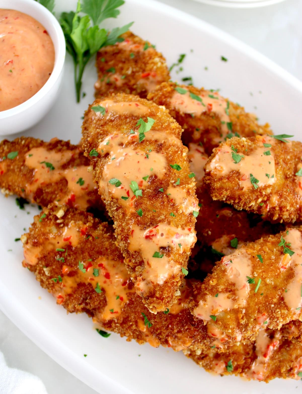 overhead view of Bang Bang Chicken Tenders on white plate with sauce on side
