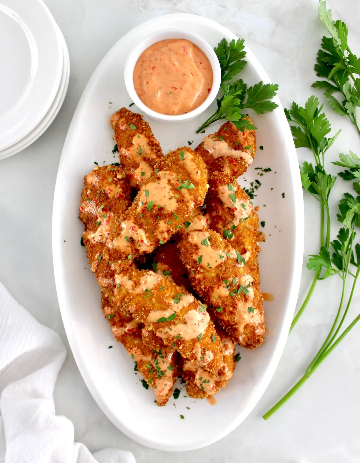 overhead view of Bang Bang Chicken Tenders on white oval platter with sauce in cup