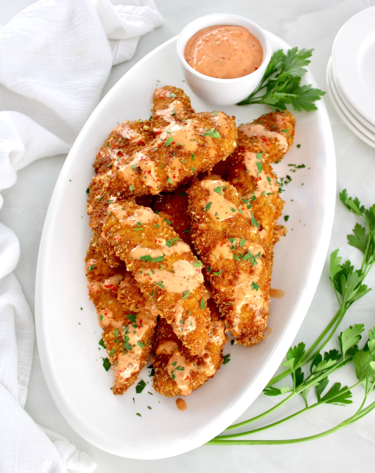 overhead view of Bang Bang Chicken Tenders on white oval plate with sauce in cup