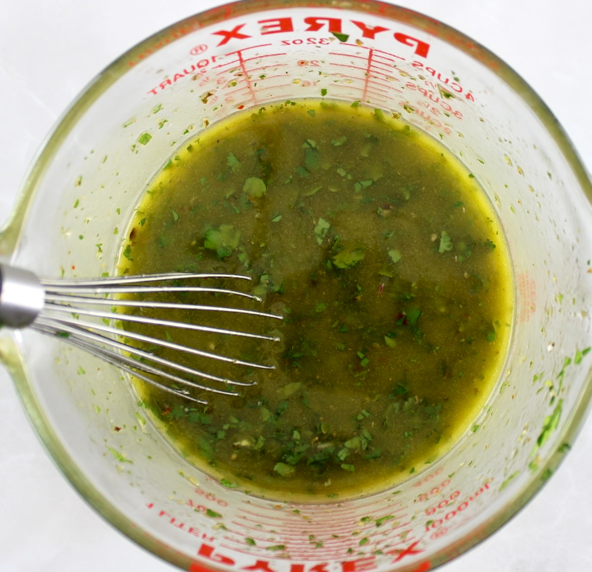 Chimichurri sauce in glass mixing bowl with whisk