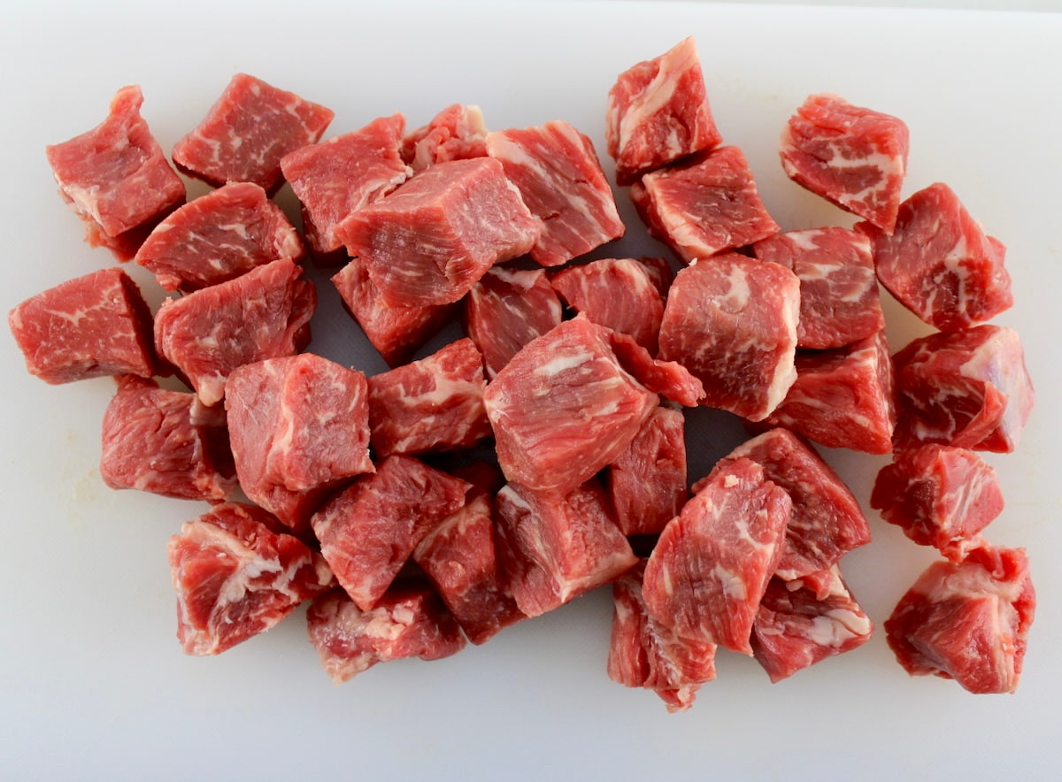 NY strip steak cut into cubes on white cutting board