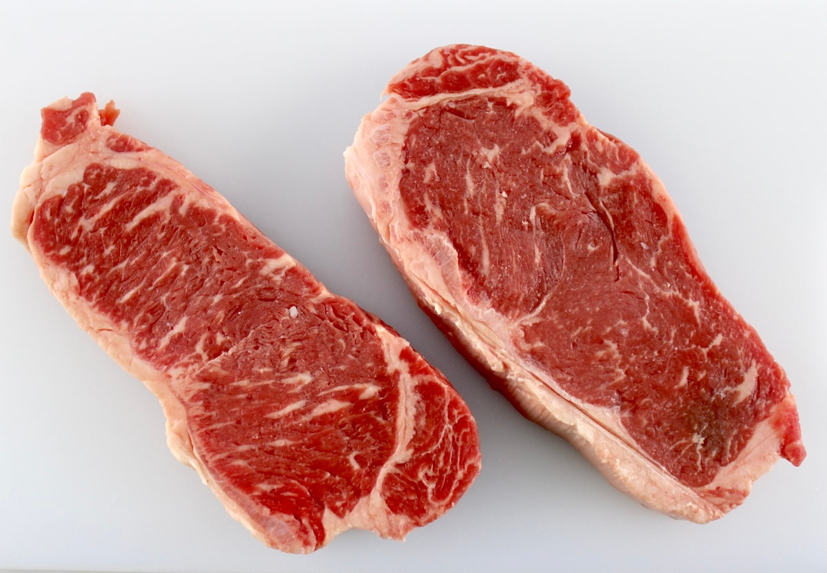 2 NY strip steaks on white cutting board