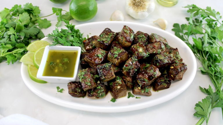 Chimichurri Steak Bites on oval white plate with sauce and lime slices on side