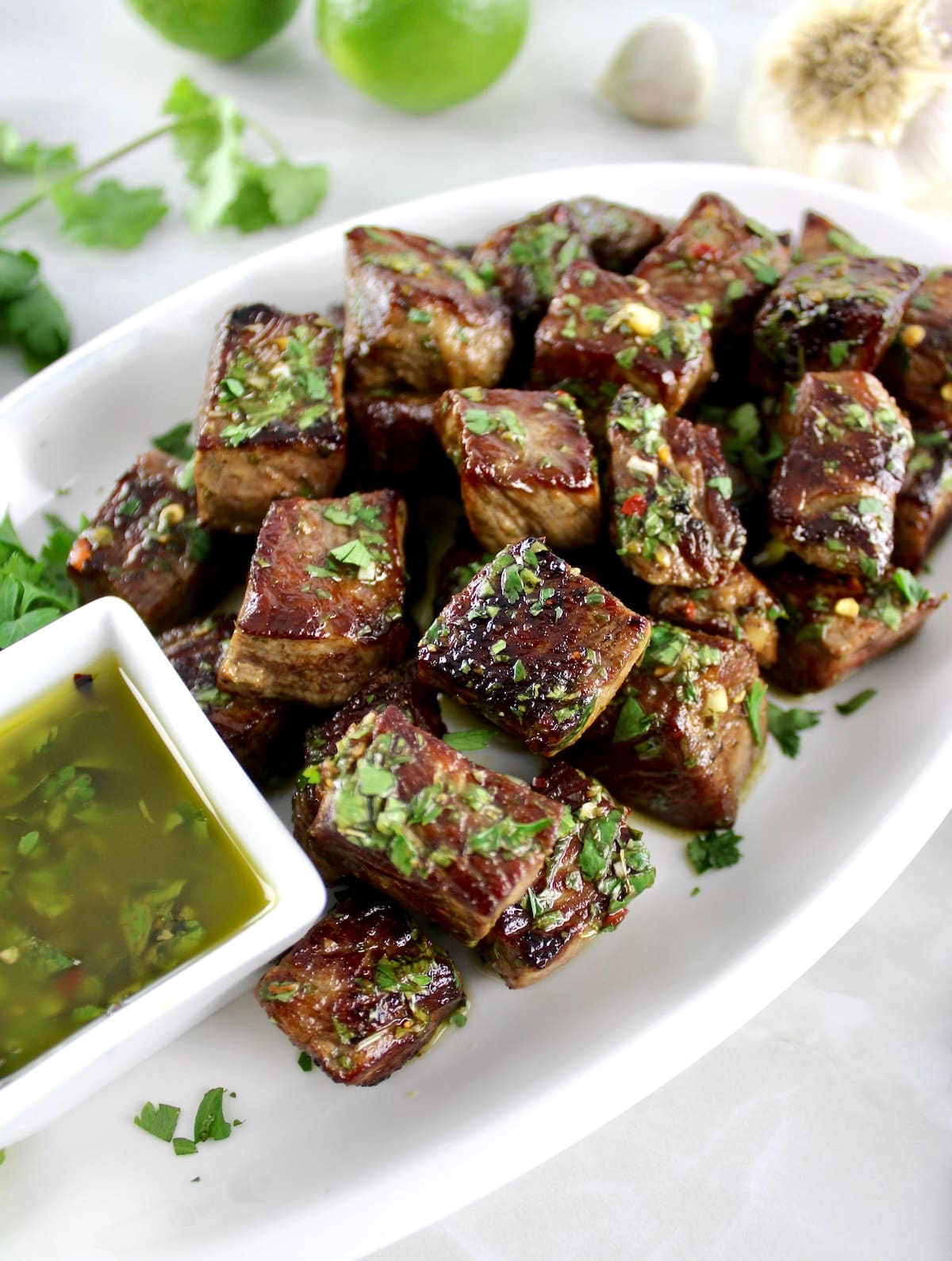 Chimichurri Steak Bites on white platter with sauce on side