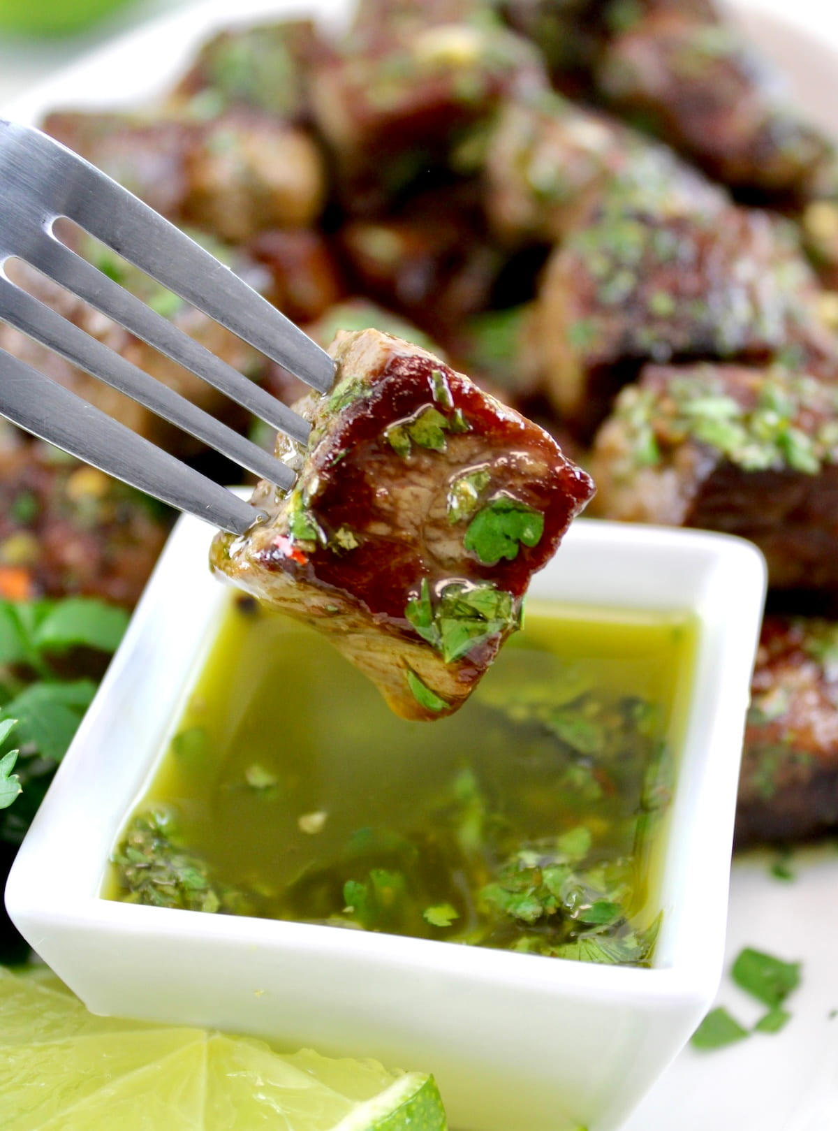 closeup of Chimichurri Steak Bite on fork held over sauce in white cup