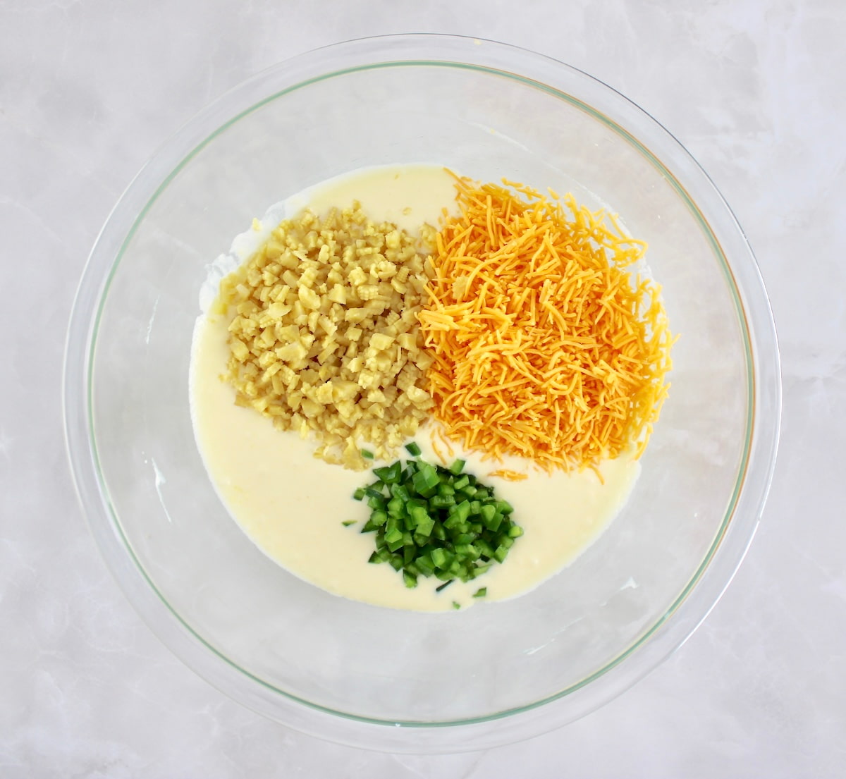 Keto Cheddar Jalapeño Cornbread batter with chopped baby corn, shredded cheddar and diced jalapeño peppers on top