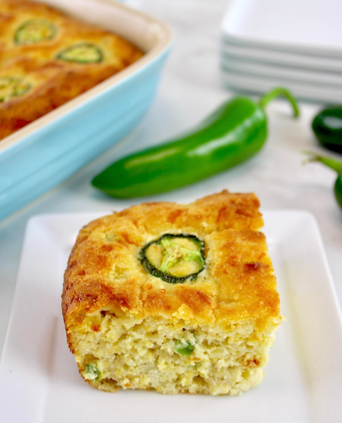 slice of Keto Cheddar Jalapeño Cornbread on white plate with casserole in back