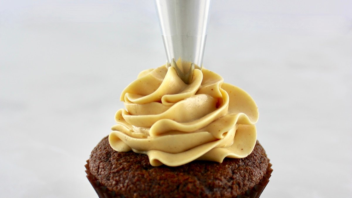 Keto Peanut Butter Frosting being piped onto chocolate cupcake