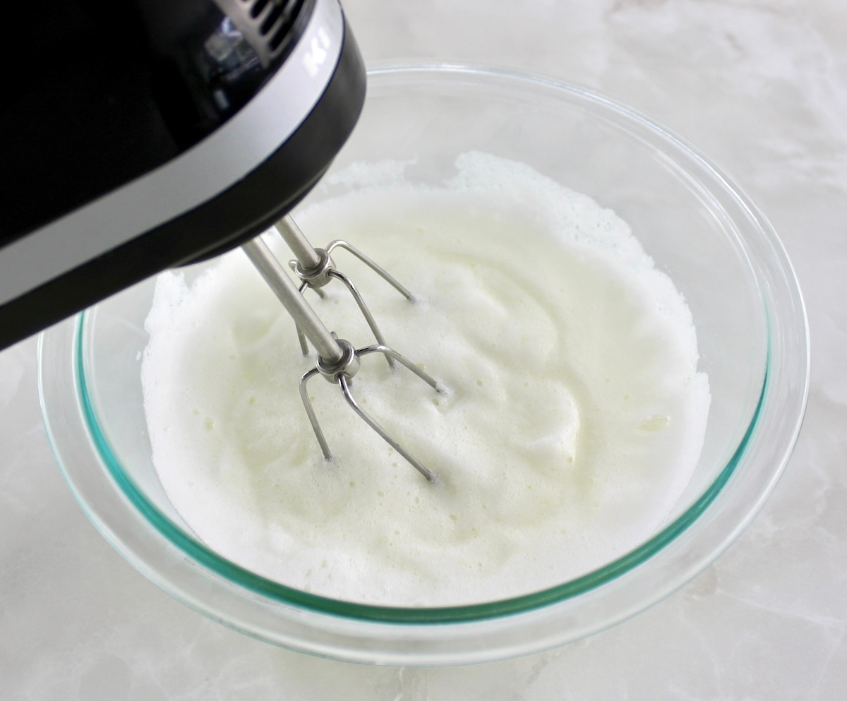 egg whites in glass bowl being whipped with hand mixer
