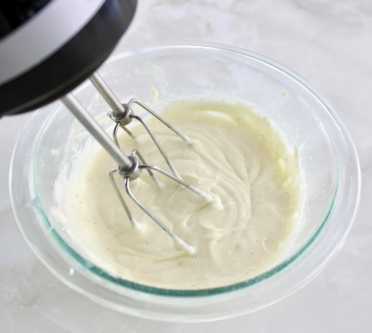 Keto Pumpkin Donuts frosting being mixed with hand mixer in glass bowl