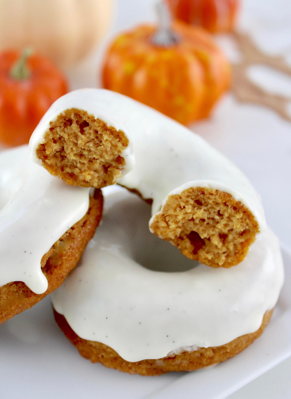 2 Keto Pumpkin Donuts stacked with one cut in half and pumpkins in back