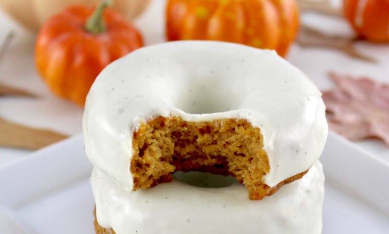 2 Keto Pumpkin Donuts stacked with bite taken out of top donut with pumpkins in back