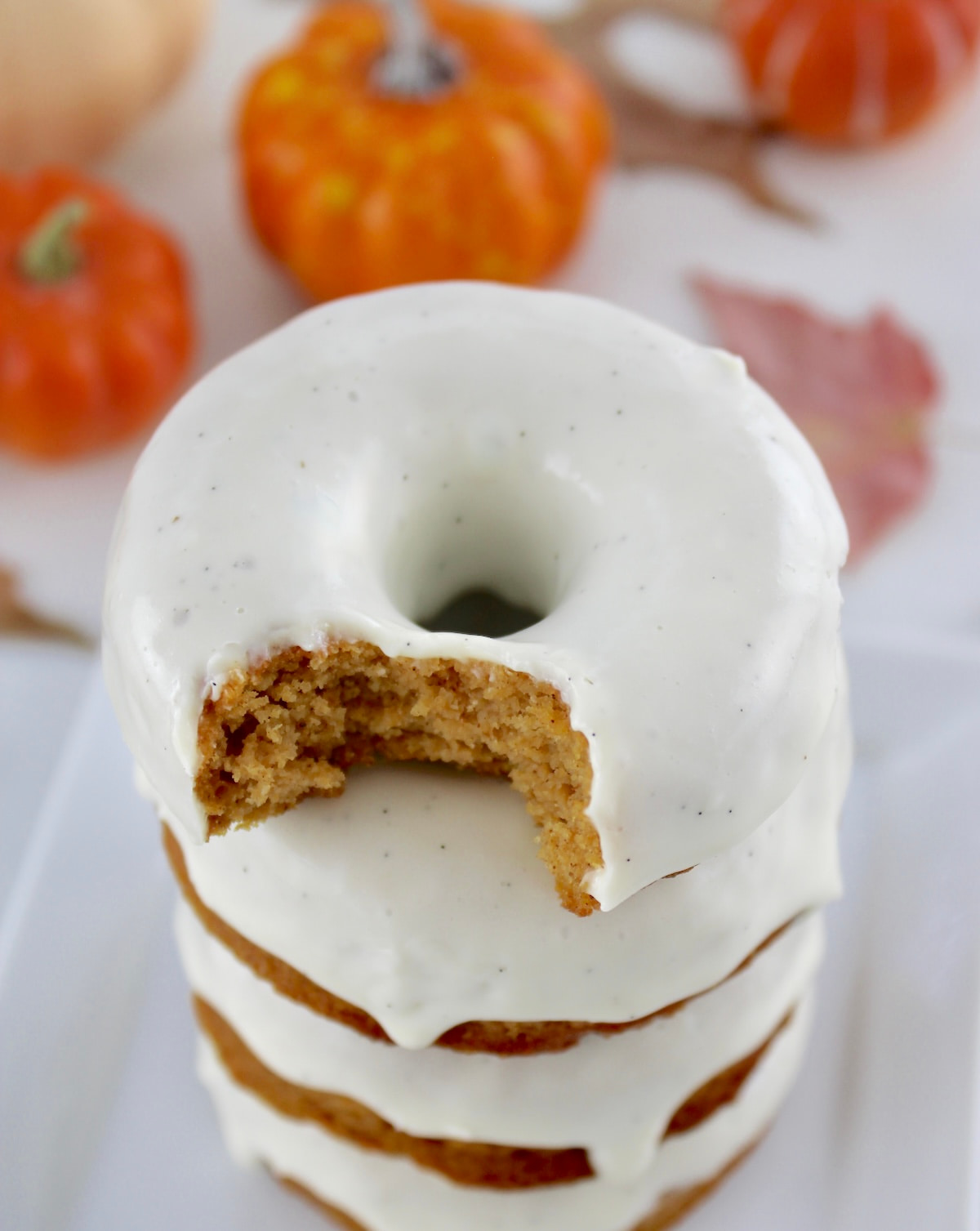 overhead view of Keto Pumpkin Donuts stacked up with bite missing from top donut and pumpkins in back