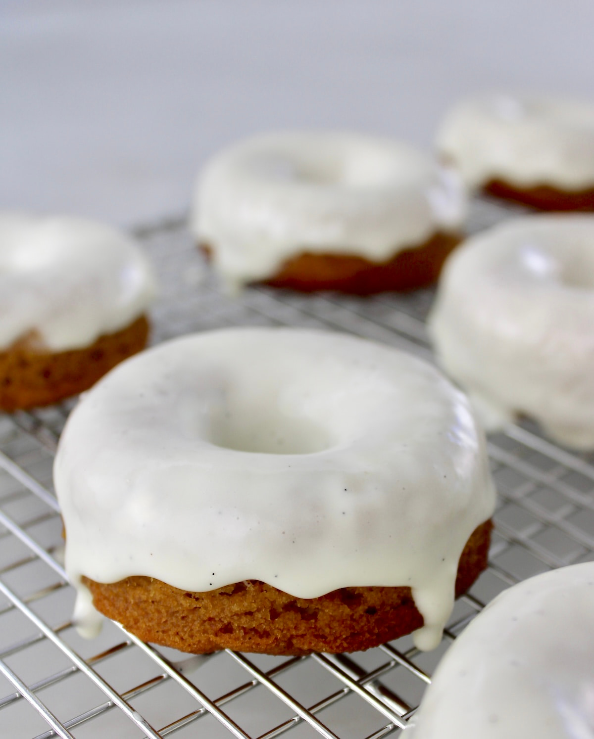 closeup of Keto Pumpkin Donuts with vanilla glaze dripping on cooling rack