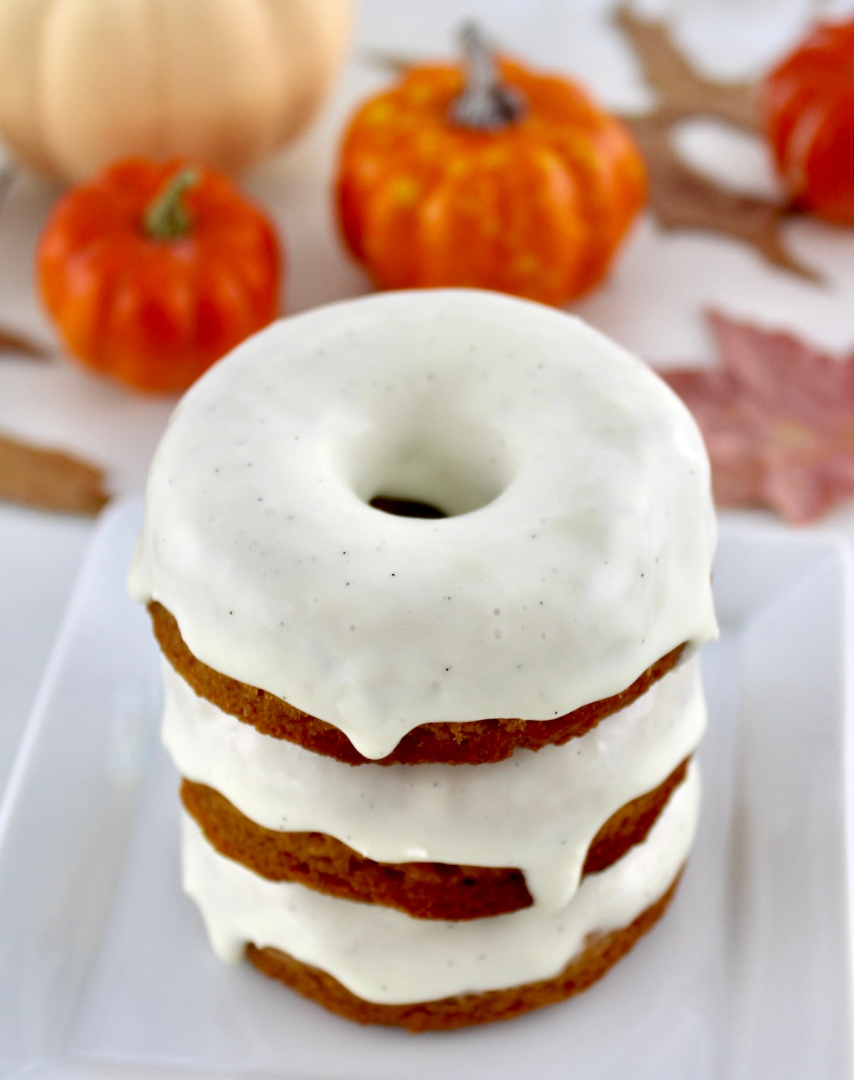 Keto Pumpkin Donuts stacked up with frosting on top and pumpkins in back