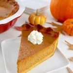 slice of Keto Pumpkin Pie on white plate with pumpkins in back
