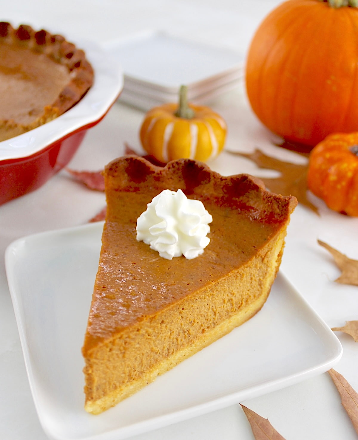 slice of Keto Pumpkin Pie on white plate with pumpkins in back