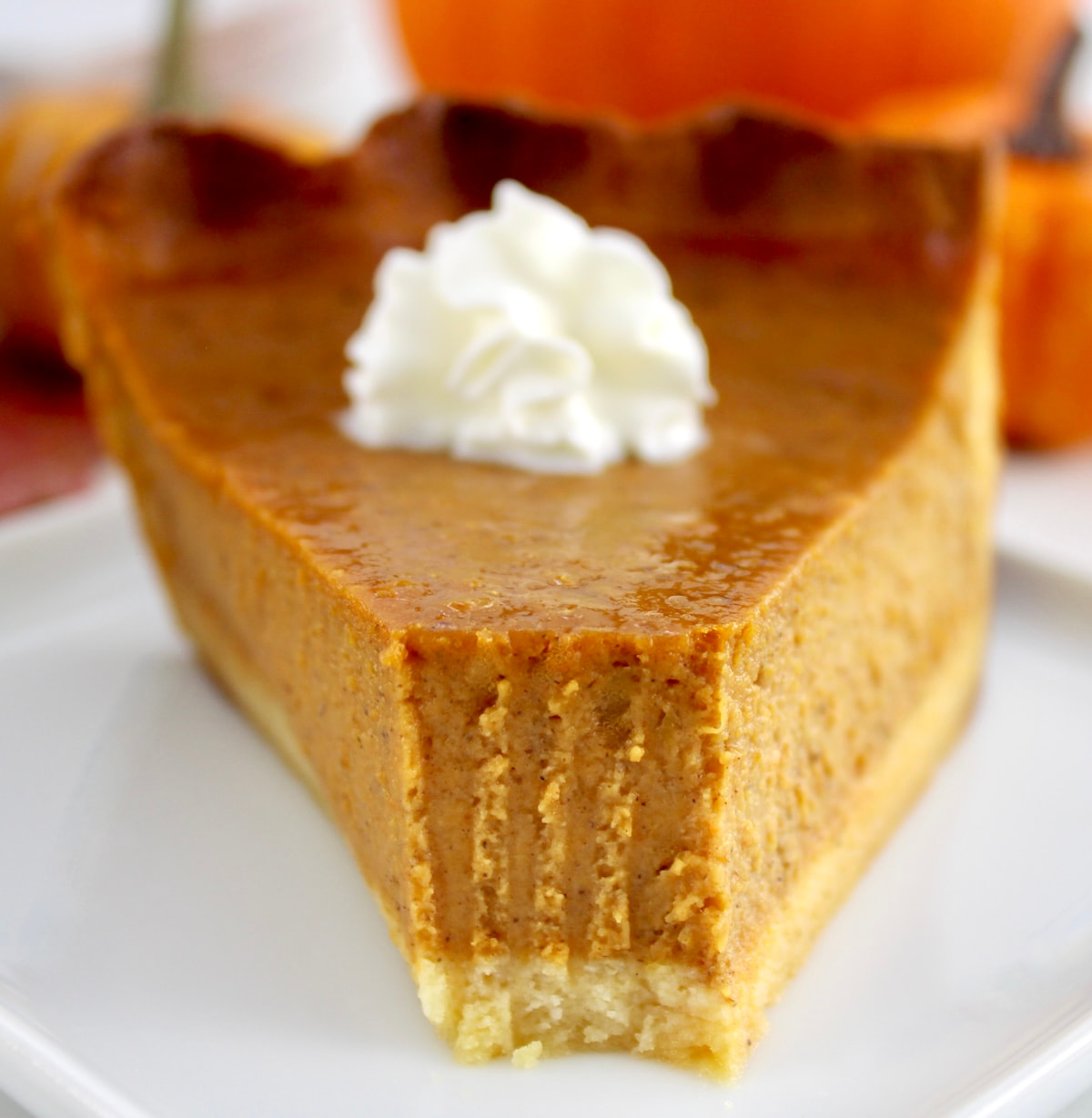 closeup of slice of Keto Pumpkin Pie on white plate with whip cream on top