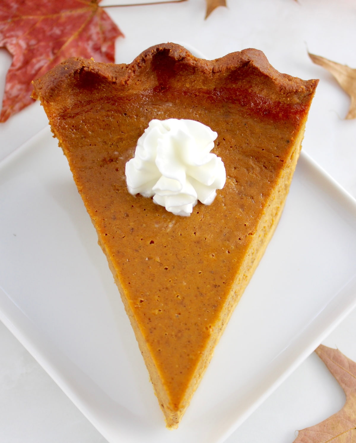 overhead view of Keto Pumpkin Pie slice on white plate with whip cream on top