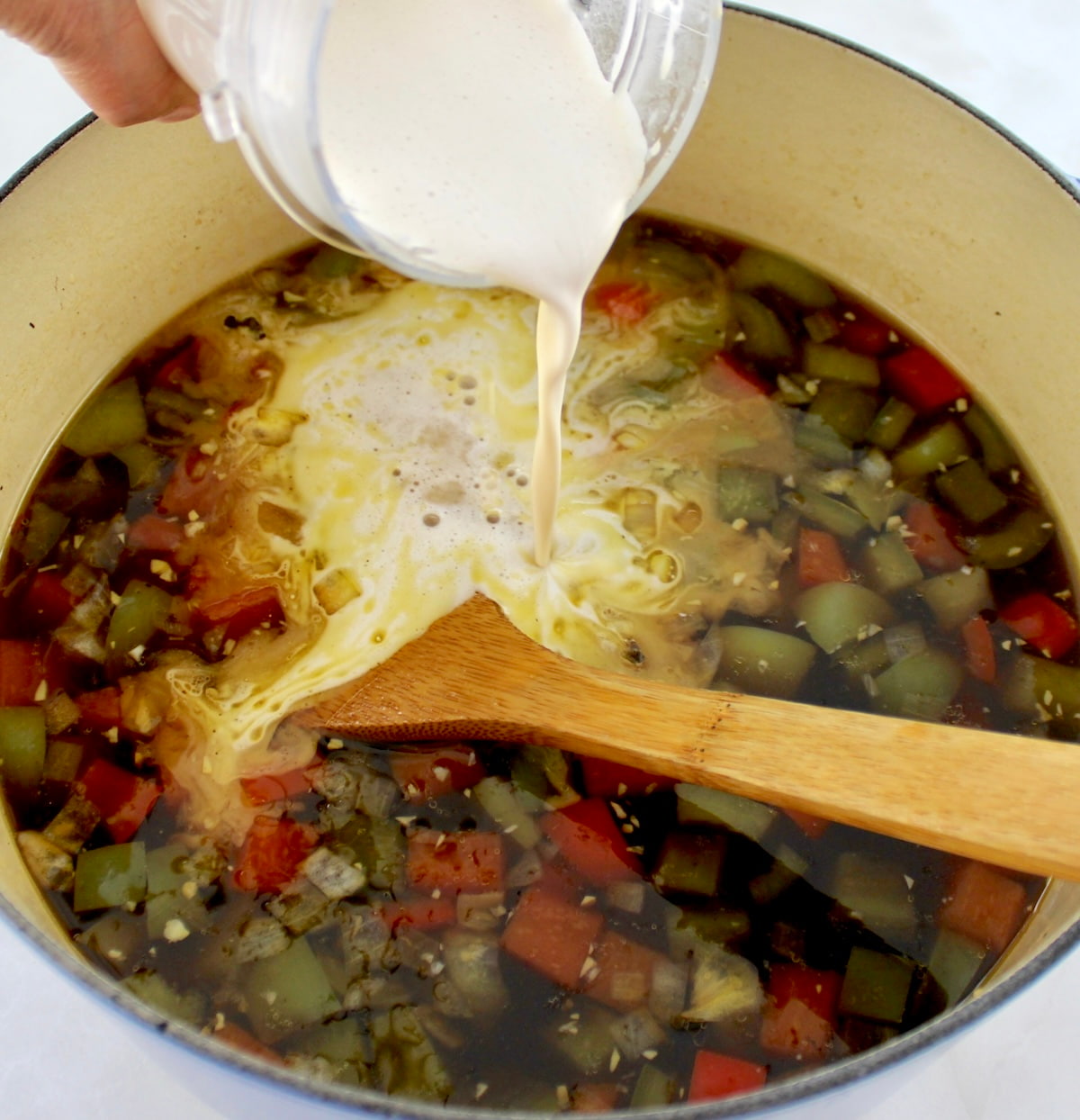 cream being poured into Philly Cheesesteak Soup in dutch oven