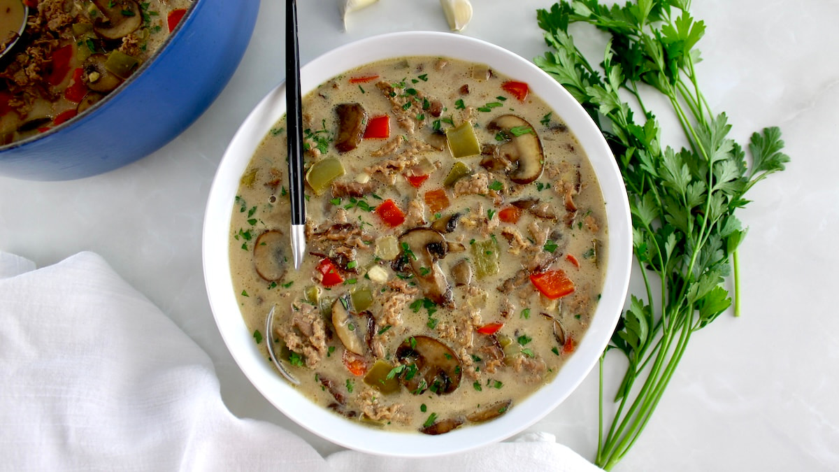 overhead view of Philly Cheesesteak Soup in white bowl with spoon on side