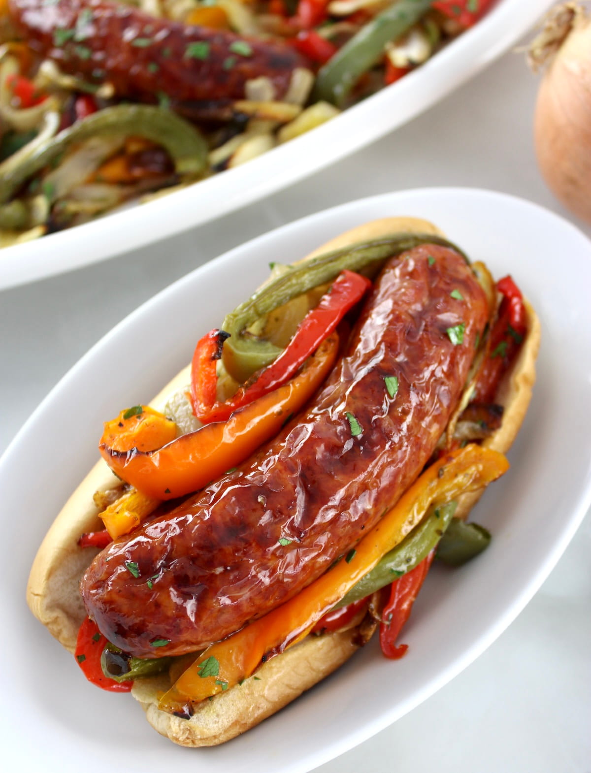 overhead view of Sheet Pan Sausage and Peppers in bun on white plate