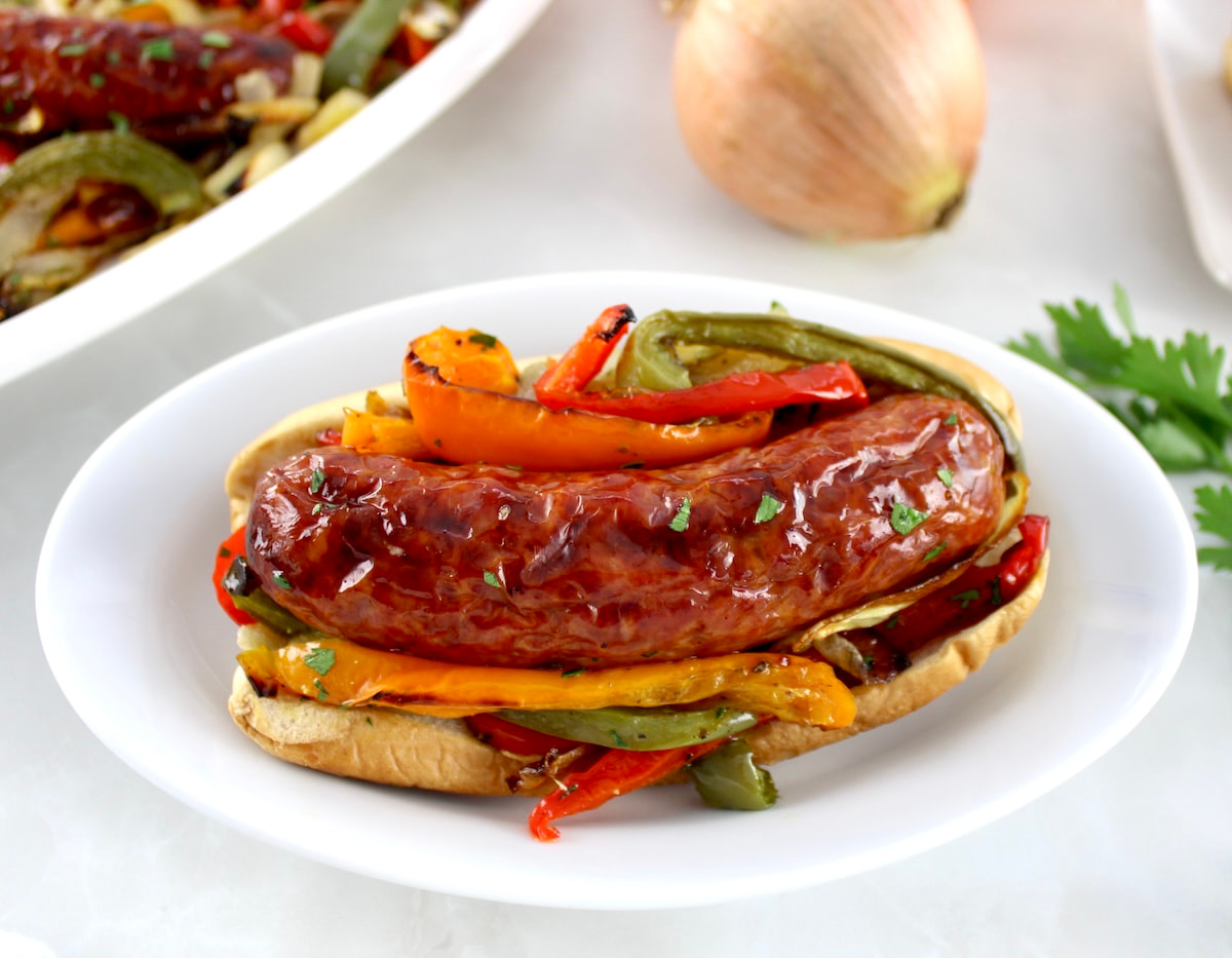 closeup of Sheet Pan Sausage and Peppers in bun on white oval plate