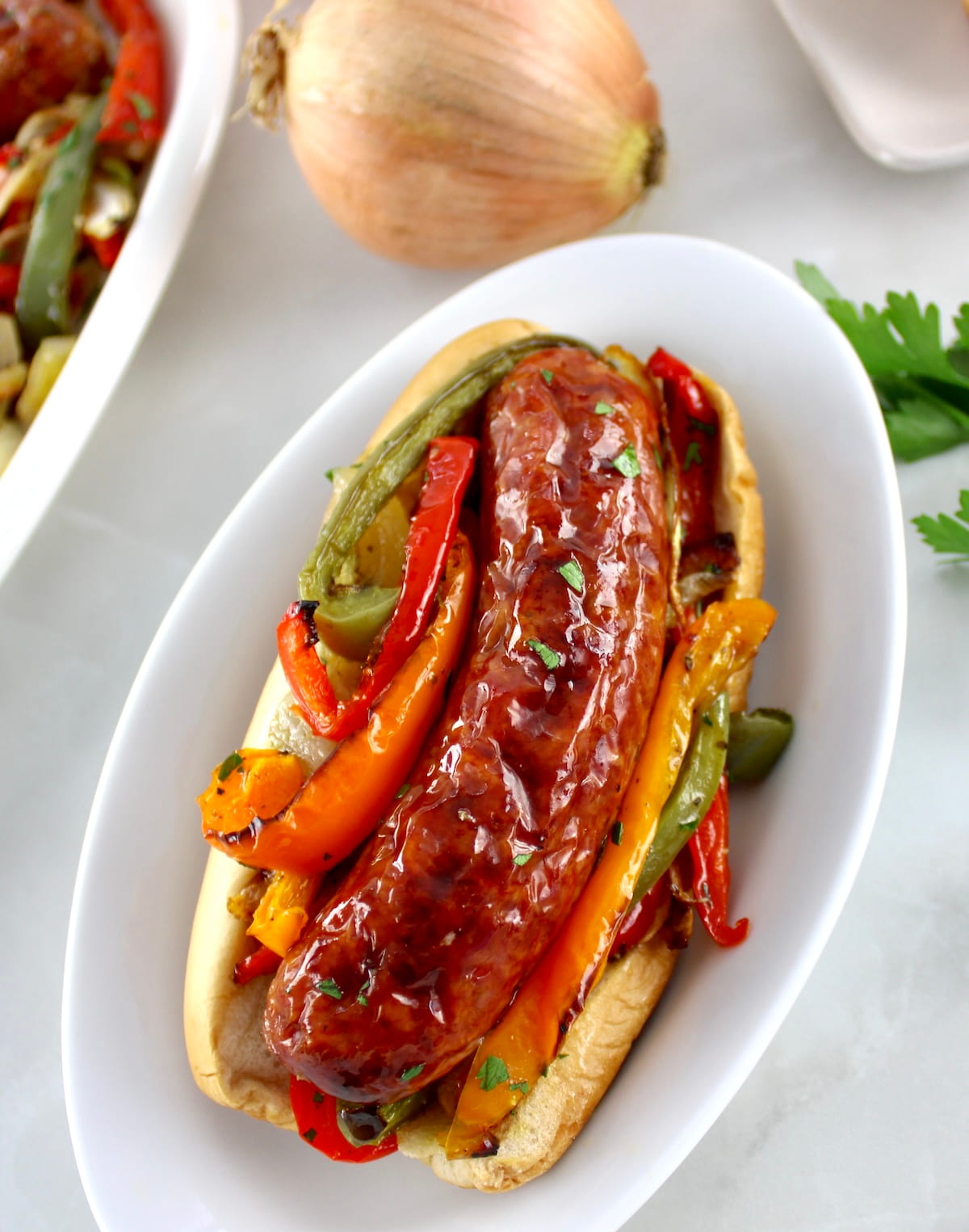 Sheet Pan Sausage and Peppers in bun on white oval plate