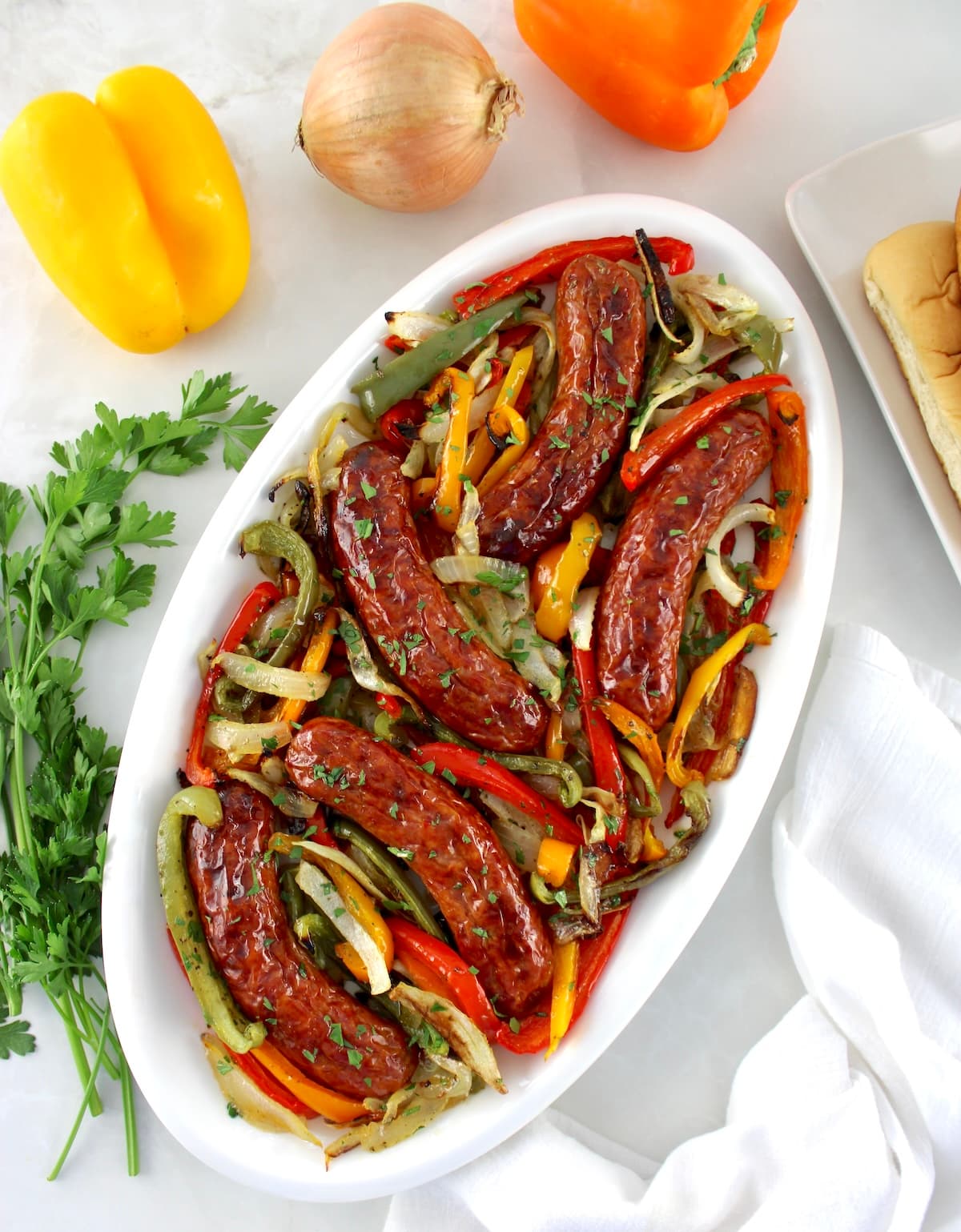 overhead view of Sheet Pan Sausage and Peppers on white oval platter with peppers in back