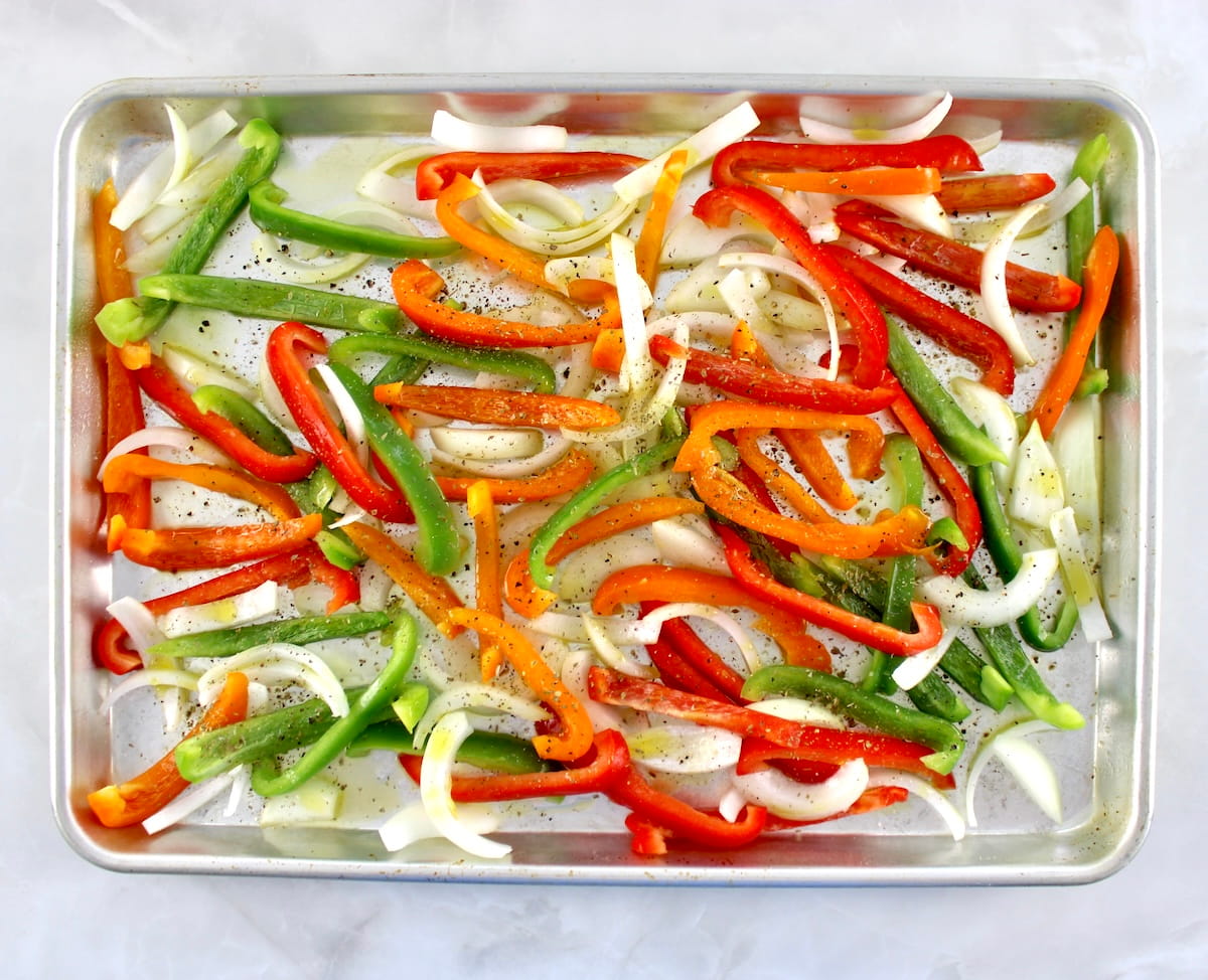 sliced bell peppers and onions  with salt, pepper and olive oil on baking sheet