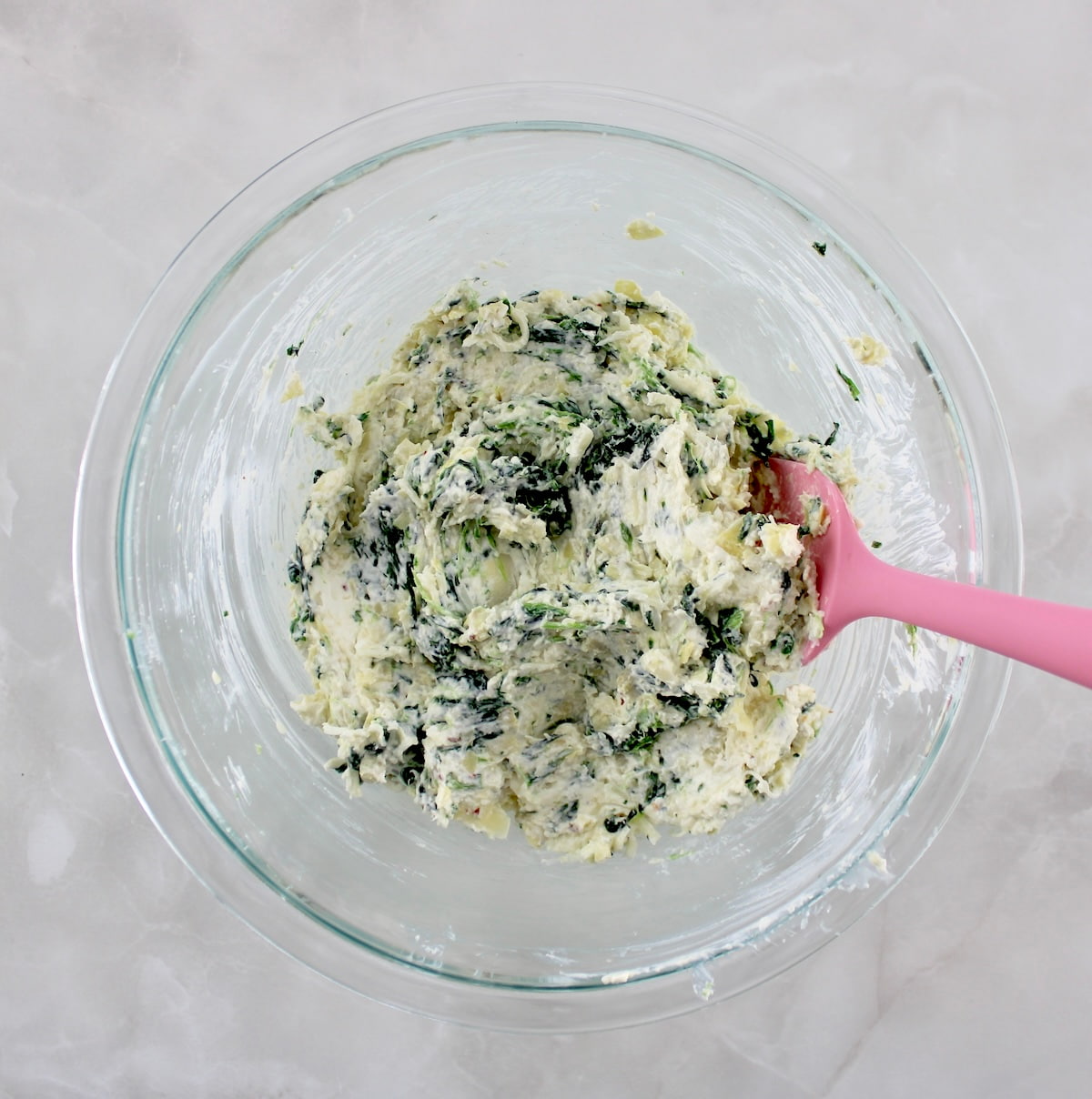 spinach artichoke filling in glass bowl with pink spoon