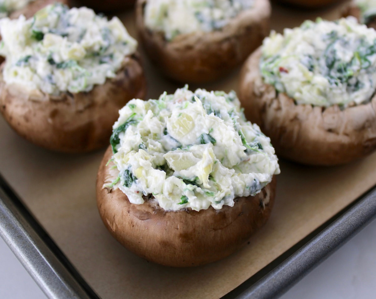 Spinach Artichoke Stuffed Mushrooms unbaked in sheet pan with parchment paper