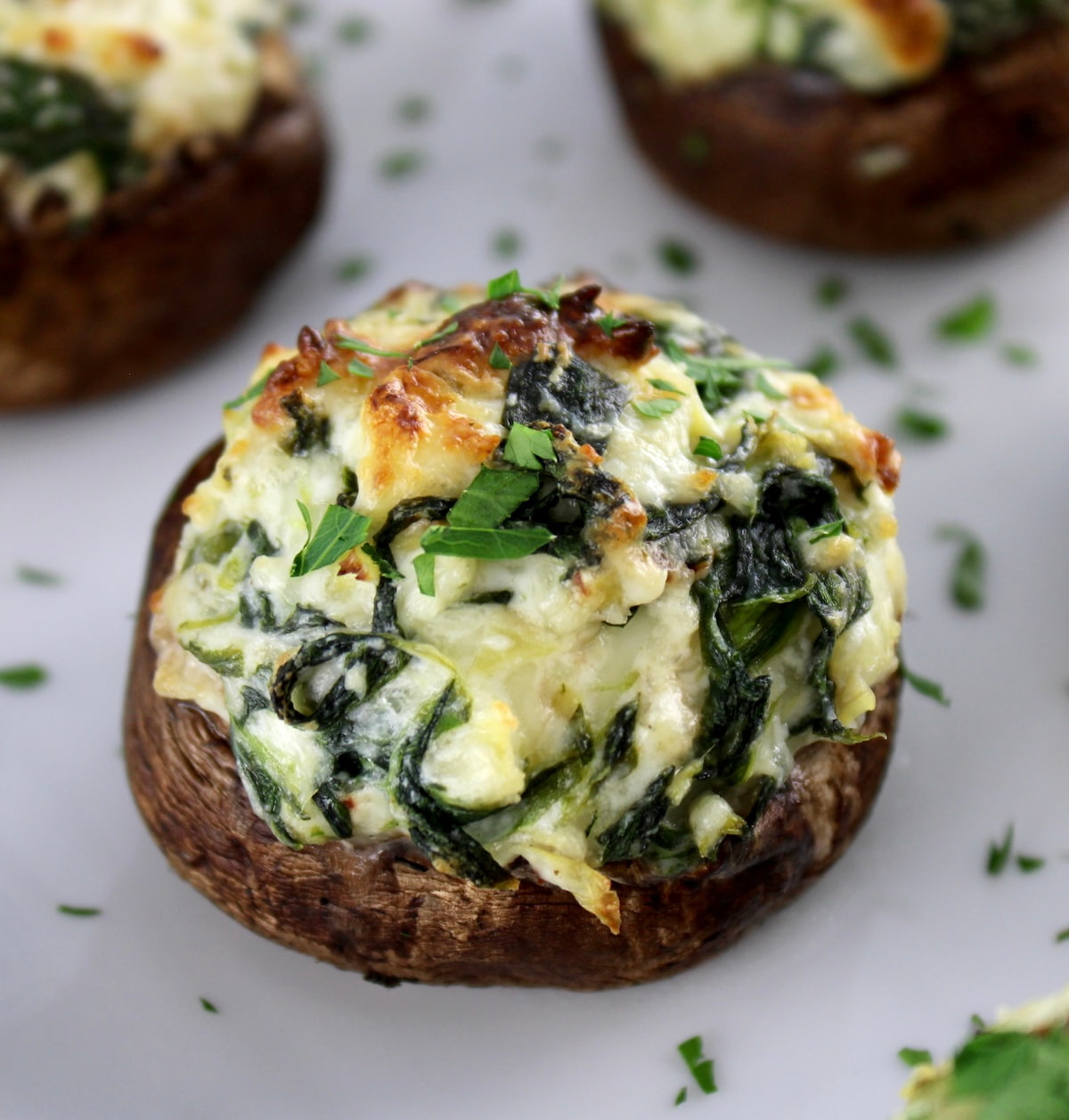 closeup of Spinach Artichoke Stuffed Mushrooms on white plate with parsley
